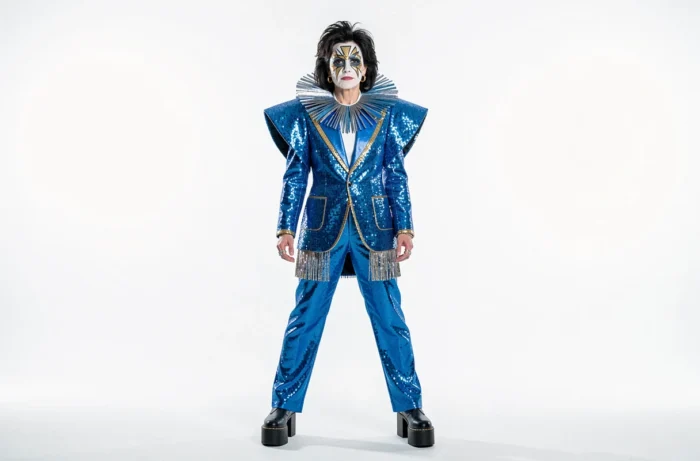 Personnage androgyne en costume glam rock bleu électrique et maquillage géométrique évoquant l'art du personnage-vêtement de David Bowie