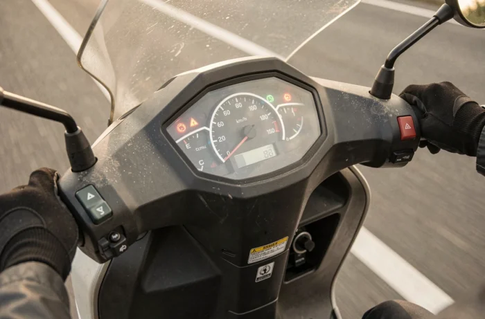 Tableau de bord d'un scooter indiquant 100 km/h sur autoroute, mains gantées du conducteur sur le guidon